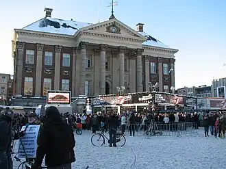 Glass house with sign and spectators, in front of city hall