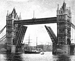 A black and white photograph of a ship sailing below a drawn up bridge