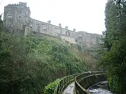 A two-storey castle with a two-storey circular tower on the left and a three-storey octagonal tower on the right. The castle overlooks a green lawn.