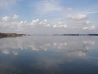 Vast lake under grey clouds with distant wooded banks.