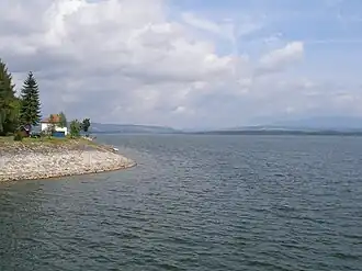A calm lake reflects distant mountains under clouds