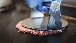 A smash burger patty being pressed on a griddle