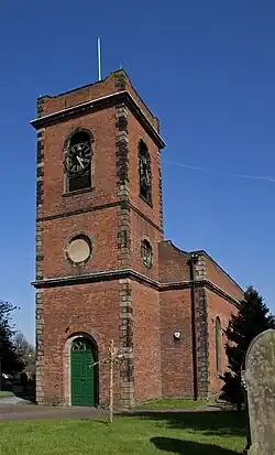 Red brick building with imposing tower having a clock and light natural quoin stone accents, many of which are pollution darkened, on a sunny day against a deep blue sky