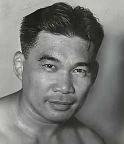 An extremely sweaty Asian man with short hair, smiling slightly toward the camera