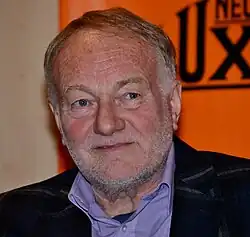 close-up of Luděk Sobota wearing a light purple shirt and dark jacket, looking left of camera with slight smile