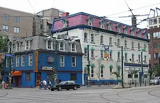 Three-storey building in the foreground painted royal blue and grey, with a four-storey building in the background painted white and pink