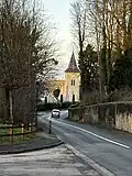 A paved road with a car drives towards St. Pierre church which is beige and has a steeple with a gray roof.
