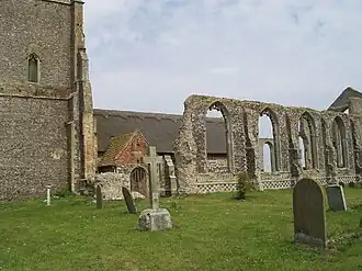 On the left the lower part of a tower, on the right the ruined wall of the aisle, and between them part of the small newer church with a thatched roof