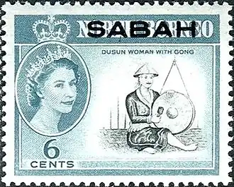 A Dusun woman[notes 1] (Kadazan woman) with a gong featured in a 1964 6¢ postage stamp of North Borneo (present-day Sabah) with a portrait of Queen Elizabeth II