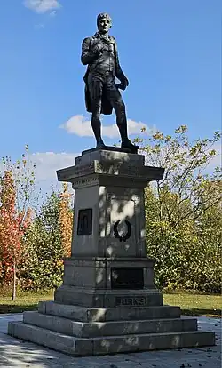 A color photograph of a statue of a standing man atop a stone pedestal