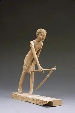 Wooden model of men bent over with a hoe.