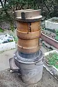 A simple hearth with a metal pan holding two wooden steaming vessels and a wooden lid used in Japan