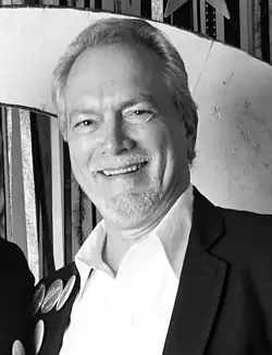 Black and white tightly-cropped photo portrait of a smiling man with gray hair and beard