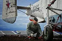 An aircraft maintenance technician inspecting a Kamov Ka-27PS on the helicopter deck, 2015