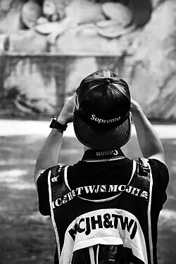 Image 66A man wearing a leather Supreme snapback hat while taking a photograph in 2016 (from 2010s in fashion)