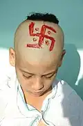 A Hindu child with a shikha and a red swastika painted on his head