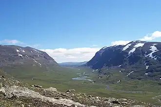 A wide view of the Syterskalet valley in northern Sweden, with a winding river between steep mountain slopes under a clear sky.