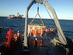 A-frame gantry over the side of a ship with a hyperbaric rescue chamber suspended over the water.