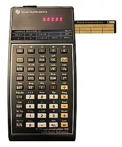 A TI-59 with a magnetic storage card being inserted into the card reader on the side.