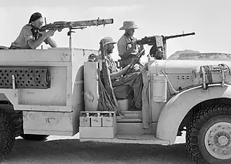 posed picture of three men one sitting in the drivers seat and the other two aiming machine guns