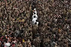 A group of devotees covered in mud gathering as a line of men in white robes travel through