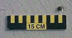 A ball of tar about 1&nbsp;cm (0&nbsp;in) wide on sand above a 15&nbsp;cm (6&nbsp;in) scale
