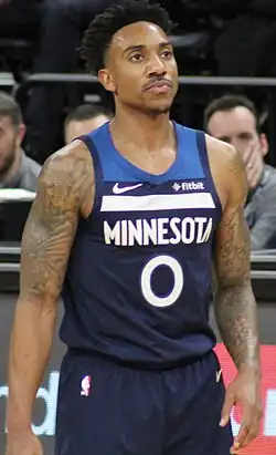 Portrait of man with dark hair and tattooed arms wearing navy blue Timberwolves uniform