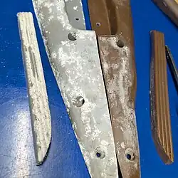 The underside of a gray plastic armrest and another brown plastic armrest. There is an obvious amount of white crystals attached, much resembling the corrosion from a dry-cell battery.