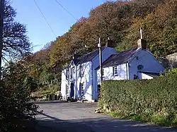 white-painted pub below wooded escarpment