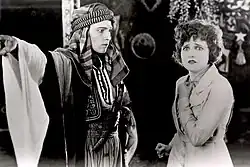 Black and white screenshot from the film The Sheik, with the man in Arab costume and the woman in Western clothing.
