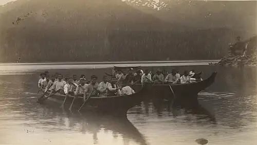 Black-and-white photograph of multiple Tlingit paddlers seated in long wooden canoes on a lake in Alaska, 1887.