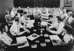 Crowded conference room. On the table are assorted petri dishes with moulds. There are graphs and tables on the blackboard behind them. A poster reads: "Buy War Bonds".