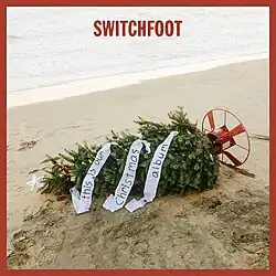 A sad sideways Christmas tree near the shore of a beach with the word SWITCHFOOT.