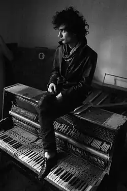 Hamasyan sitting atop an opened upright piano (facing southwest); black-and-white photo, 2009