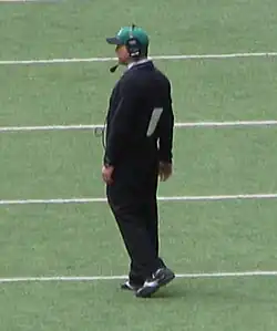A horizontal photograph of a man standing on a football field