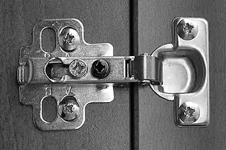 Door in furniture with spring to hold door either fully shut or fully open. It hides completely behind the door and has adjustment for fine alignment. Allows the door to open even when against a wall.