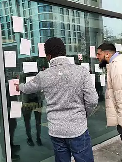 Onlookers read fake birth, death, and marriage certificates stuck to the Tŷ William Morgan building. One onlooker points at a page.