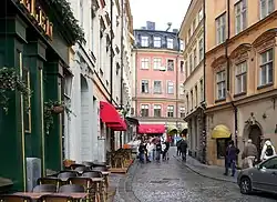 An alley paved with stones curves slightly to the right, with cafes on the left side, 4 storey buildings on the left.