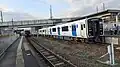 A photograph of BEC819 series in Doi Station (Fukuoka) with 2 trains on Kashii Line headed towards opposite sides, towards Umi Station (closest train; heading towards right of image) and presumably Kashii Station/Saitozaki Station.