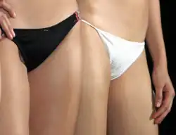 Two women; one is wearing black conventional bikini underwear and the other is wearing white string bikini underwear.