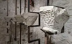 A series of carved column pieces with floral and scroll motifs are showcased in a basement.