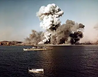A warship observes as a port explodes in the background
