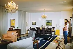 The interior of a US consulate, showing a sitting room and various guests.