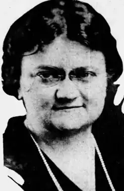 A white woman with dark hair, wearing glasses and a strand of pearls