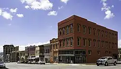 A group of buildings with vehicles parked in front line a downtown street