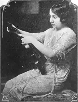 A young woman with dark hair, seated, holding a violin