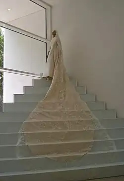 A mannequin wearing a beige wedding dress at the top of corner-stairs with the bridal veil draping down the steps