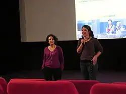 Two women stand in front of a screen in a movie theater