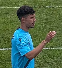 Right profile of a man in a blue shirt with left hand raised