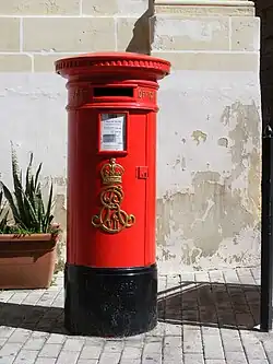 A red pillar box in Vittoriosa, Malta. In the 1980s, royal cyphers were ground off the pillar boxes in Valletta and Floriana, but most others remained intact.[29]